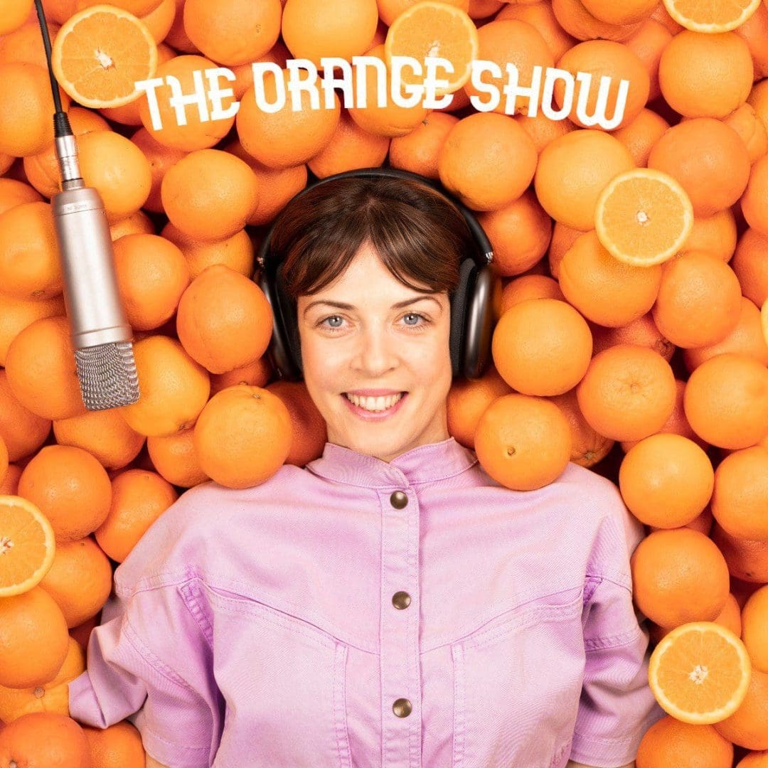 H Έρρικα Ρούσσου ξαπλωμένη σε πορτοκάλια ακούει το podcast «The Orange Show»